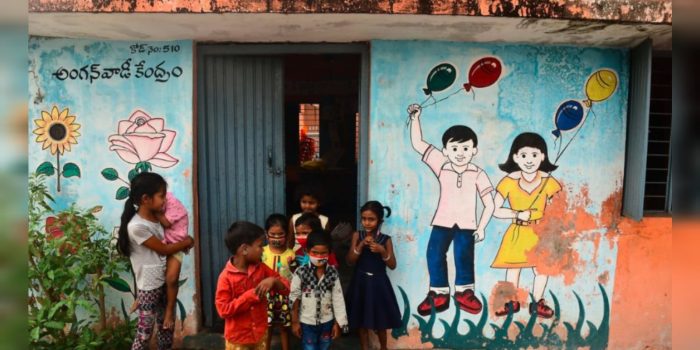 Image of an Anganwadi centre with colourful walls and children standing in front of it